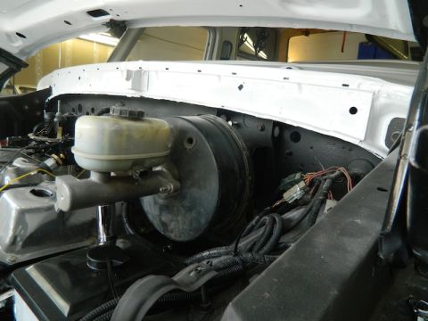 1979 Ford Bronco - Close-up of a brake booster and master cylinder in a white vehicle's engine bay.
