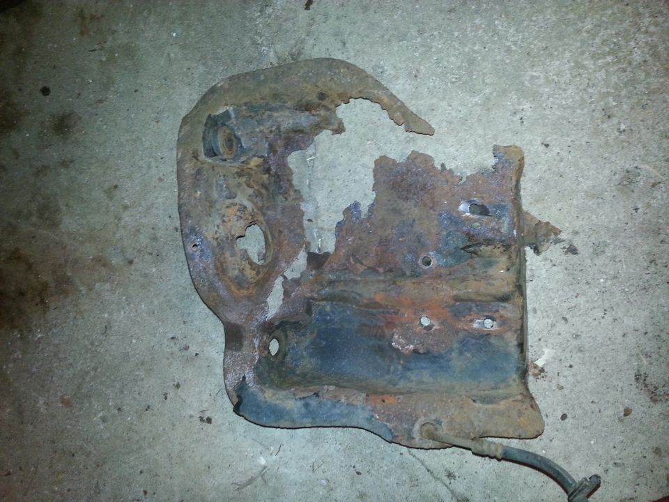 Heavily rusted and damaged metal bracket with holes and torn edges, lying on a concrete surface