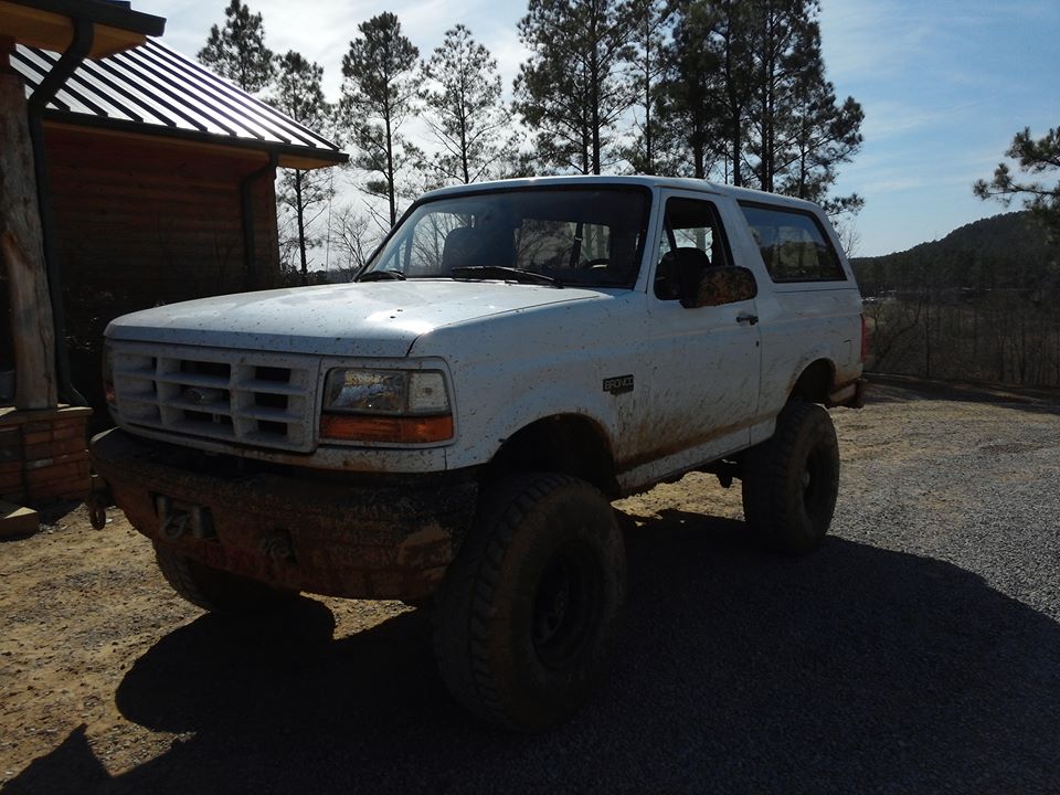 1995 Ford Bronco with lifted suspension and aftermarket front bumper, parked near a wooden building