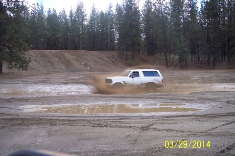 1990 Ford Bronco - 1990 Ford Bronco navigating a muddy terrain with trees in the background.