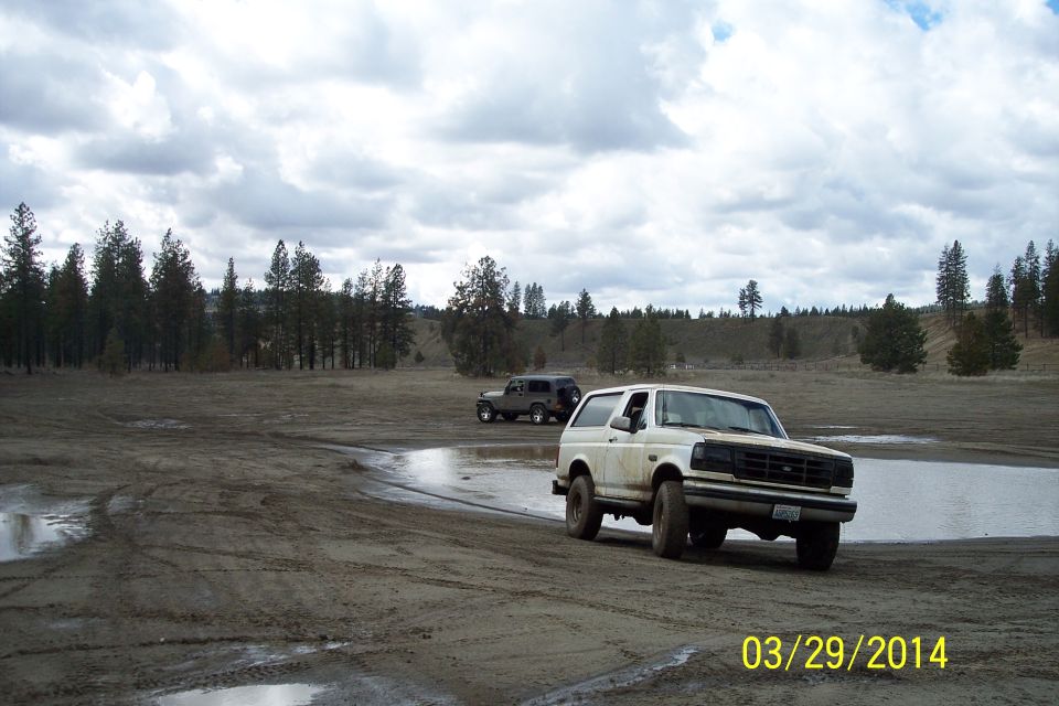 White Ford Bronco driving on dirt near water, another SUV behind it