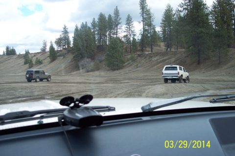 1990 Ford Bronco - A white 1990 Ford Bronco is seen from the interior of another vehicle, driving on a dirt road with a second SUV in the distance.