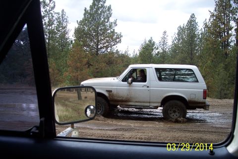 1990 Ford Bronco - A white 1990 Ford Bronco navigates a muddy track surrounded by trees.