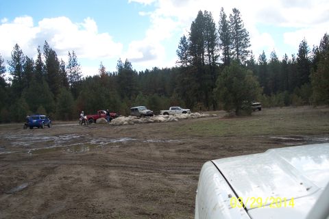 1990 Ford Bronco - Multiple vehicles are gathered in a muddy, wooded area, suggesting an off-road excursion.