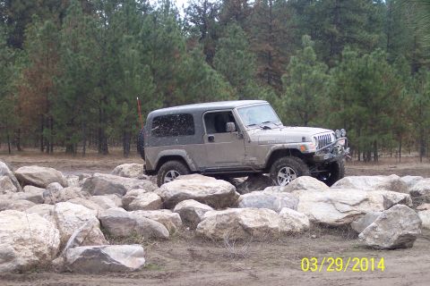 1990 Ford Bronco - Jeep Wrangler Rubicon navigating a rocky obstacle course in a wooded area.
