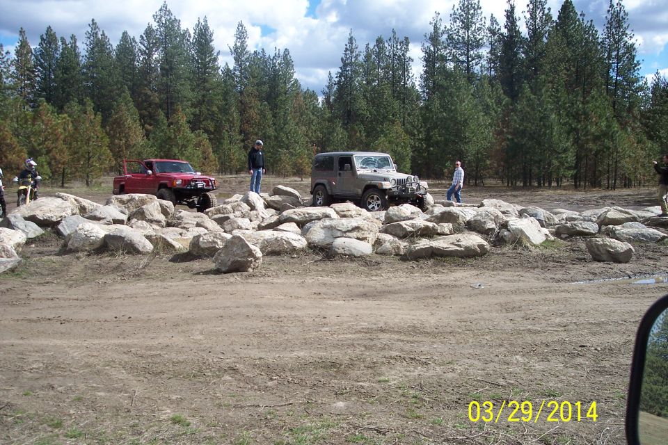 Red pickup truck and silver Jeep on rocky terrain with trees in background