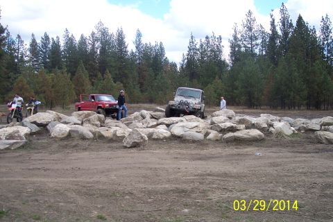 1990 Ford Bronco - Several off-road vehicles and motorcycles are gathered near a rocky obstacle course in a wooded area.