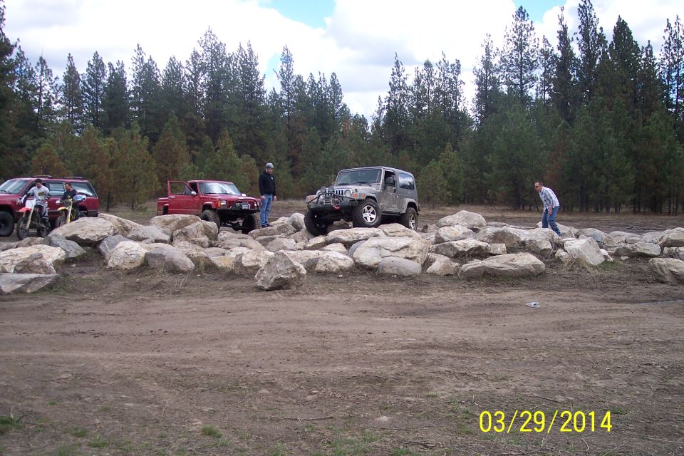 Silver Jeep Wrangler on rocks, front-right tire elevated
