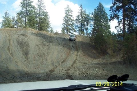1990 Ford Bronco - A white SUV navigates a challenging ascent on a dirt hill, captured from the perspective of a following vehicle.