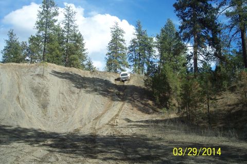 1990 Ford Bronco - SUV navigates a challenging dirt incline surrounded by trees under a partly cloudy sky.