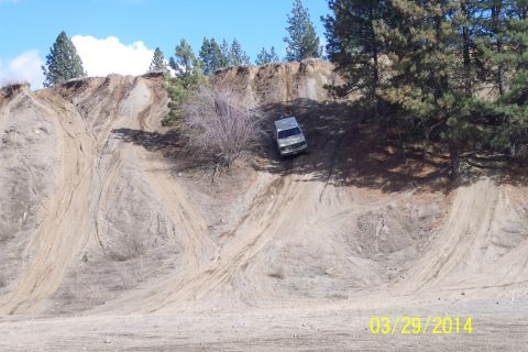 1990 Ford Bronco - A silver SUV navigates a challenging dirt incline, leaving visible tire tracks on the slope.