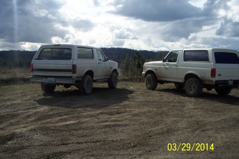 1990 Ford Bronco - Two white 1990 Ford Broncos are parked on a dirt road under a cloudy sky.