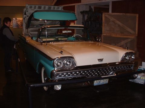 1999 Ford Crown Victoria - A vintage convertible with a retractable hardtop is displayed indoors, possibly in a museum or showroom.