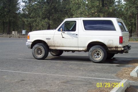 1990 Ford Bronco - This white Ford Bronco is parked in a lot with trees in the background.