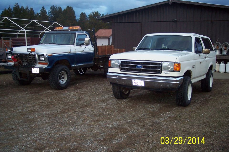 White Ford Bronco and a blue and white tow truck parked on gravel
