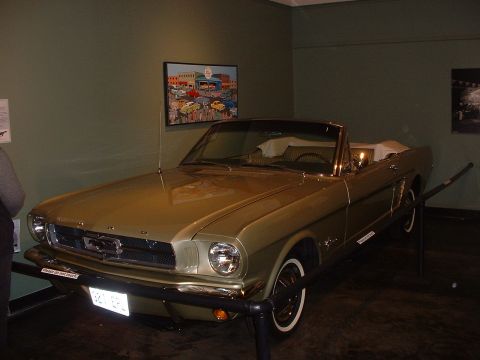 1999 Ford Crown Victoria - A gold 1965 Ford Mustang convertible is displayed in a museum setting.