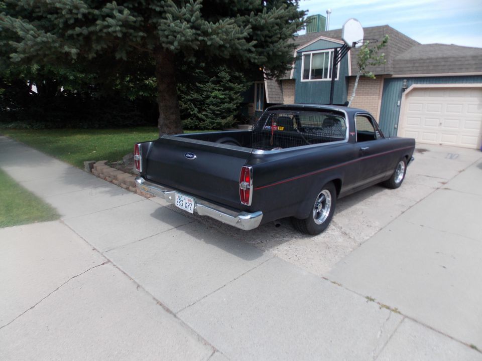 Flat black Ford Ranchero, rear three-quarter view, parked on driveway in front of a house