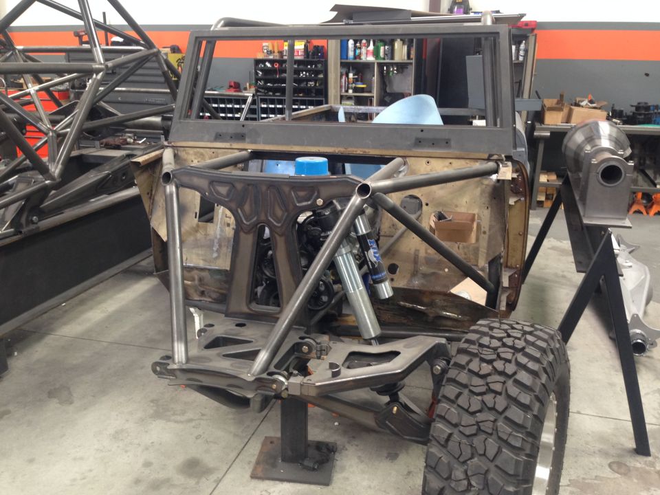 Off-road vehicle chassis with roll cage, engine, and suspension components visible. It's in a workshop setting