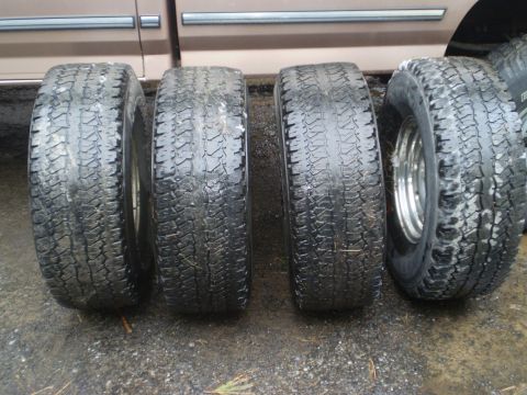 1979 Ford Bronco - Four tires are displayed on a wet surface, with the lower portion of a truck visible in the background.