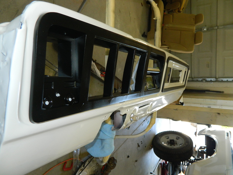 White car interior panel with black trim and louvers, undergoing restoration. A spare tire is visible