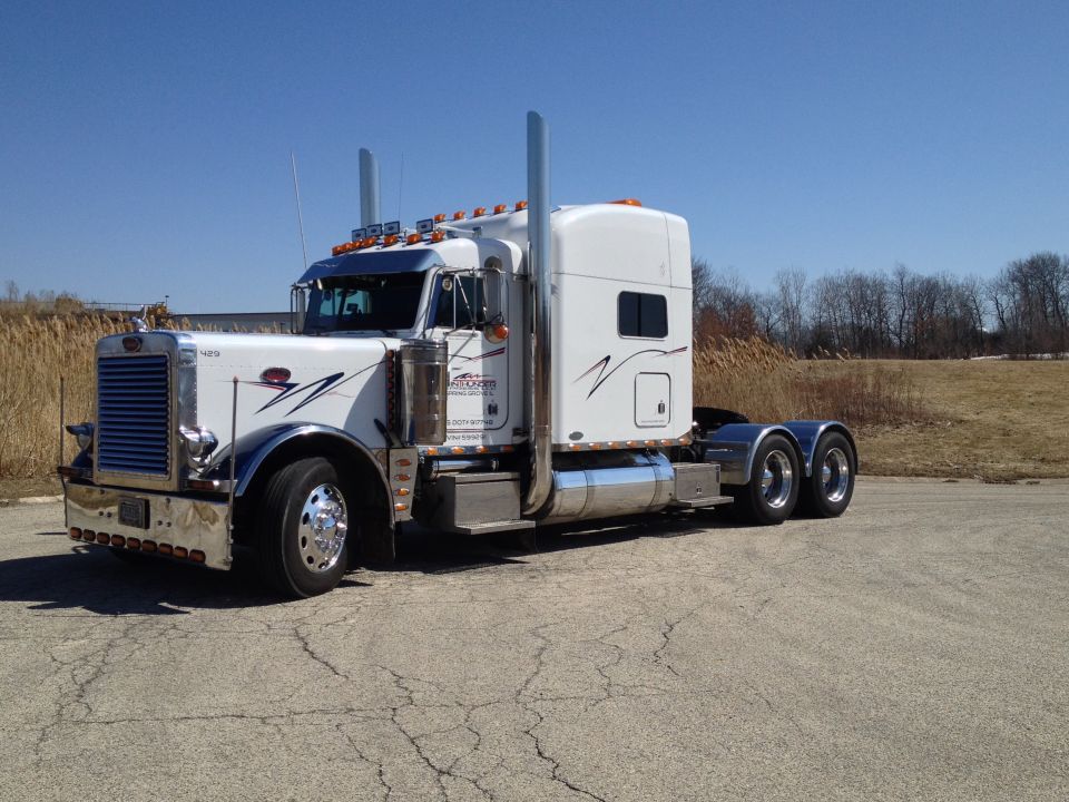 White 2003 Peterbilt 379 semi-truck with chrome accents and black pinstripes, parked on cracked asphalt