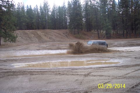 2005 Jeep Wrangler - A vehicle navigates a muddy off-road course, sending a spray of dirt into the air.