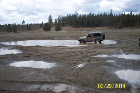 2005 Jeep Wrangler - A Jeep Wrangler navigates a wet, muddy terrain with tire tracks visible.