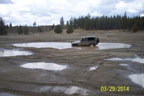 2005 Jeep Wrangler - A gray 2005 Jeep Wrangler navigates through a large muddy puddle in an open, wooded area.