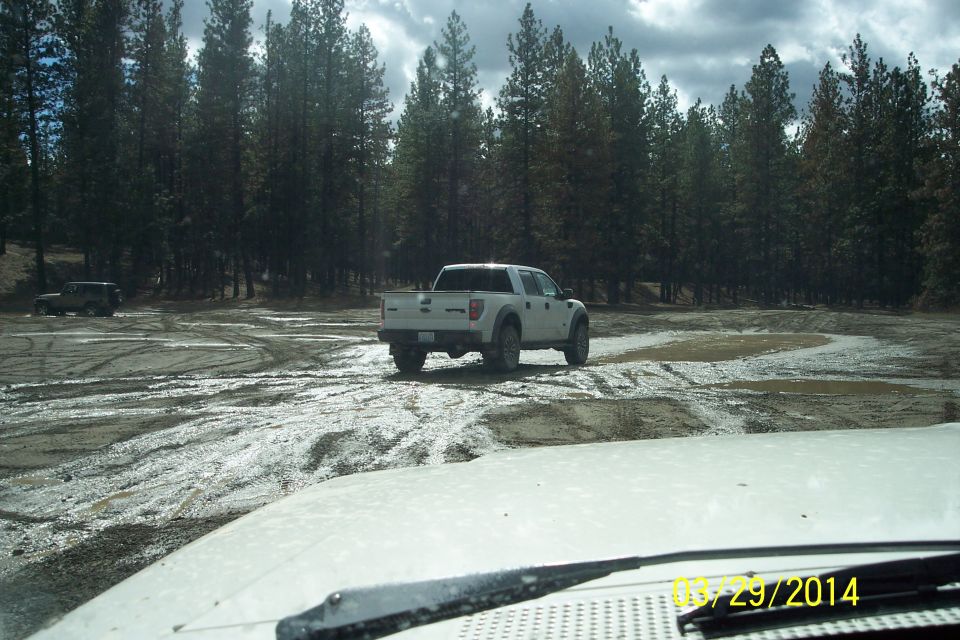 White pickup truck driving on a muddy dirt road with trees in background