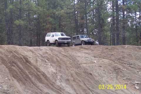 2005 Jeep Wrangler - Two off-road vehicles, a Jeep Wrangler and a Ford Bronco, are positioned on a dirt incline with a forest backdrop.