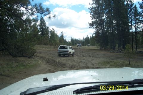 2005 Jeep Wrangler - Multiple vehicles navigate a muddy, wooded trail under a cloudy sky.