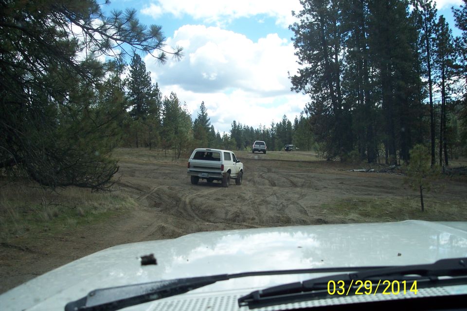 White SUV driving on a dirt road with trees and a cloudy sky