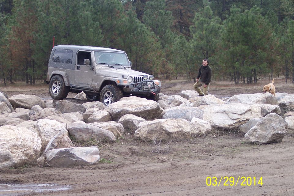 Jeep Wrangler driving over large rocks with a person and dog nearby