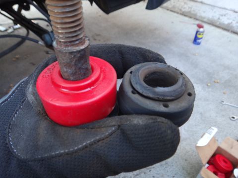1993 Ford Taurus - A gloved hand holds a new red polyurethane bushing and an old rubber bushing, likely for vehicle suspension replacement.
