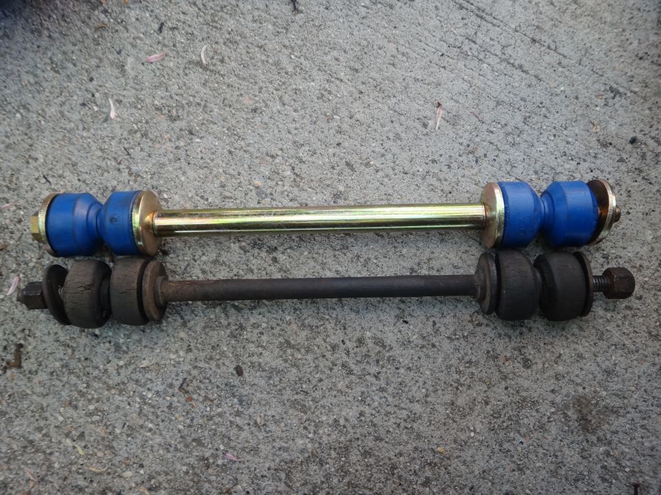 Two sway bar links on concrete; one is new with blue bushings and a gold bar, the other is old and rusted