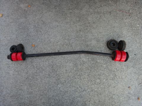 1993 Ford Taurus - Sway bar with red polyurethane bushings and black rubber mounts laid out on a concrete surface.