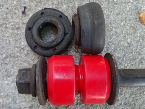 1993 Ford Taurus - Two old rubber bushings and a new red polyurethane sway bar link assembly are laid out on a concrete surface.