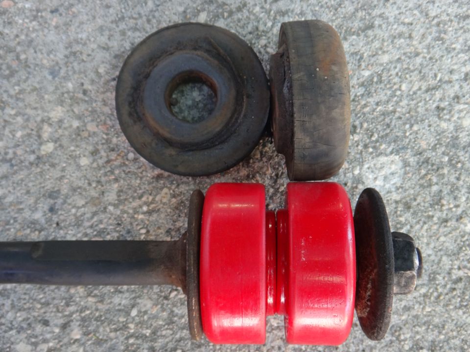 Two old black rubber bushings and one new red polyurethane bushing on a metal rod