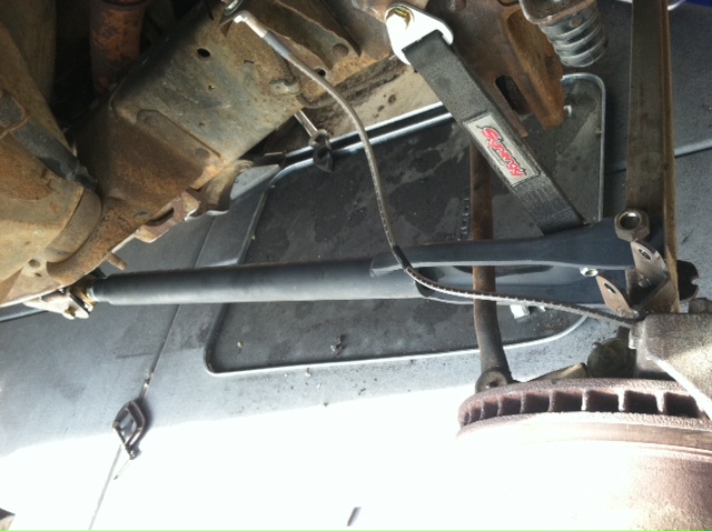 Close-up of a vehicle's suspension with a black strap and metal components visible. Supermotors.net logo at bottom right
