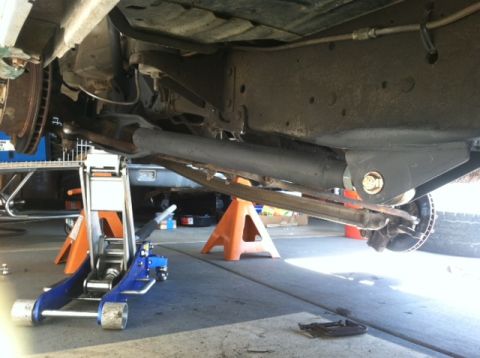 1977 Ford F-350 - The underside of a vehicle is supported by jack stands and a hydraulic jack, revealing its suspension system.