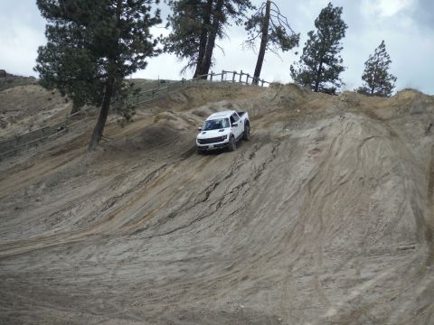 2005 Jeep Wrangler - A white pickup truck navigates a steep, muddy incline on an off-road trail under an overcast sky.