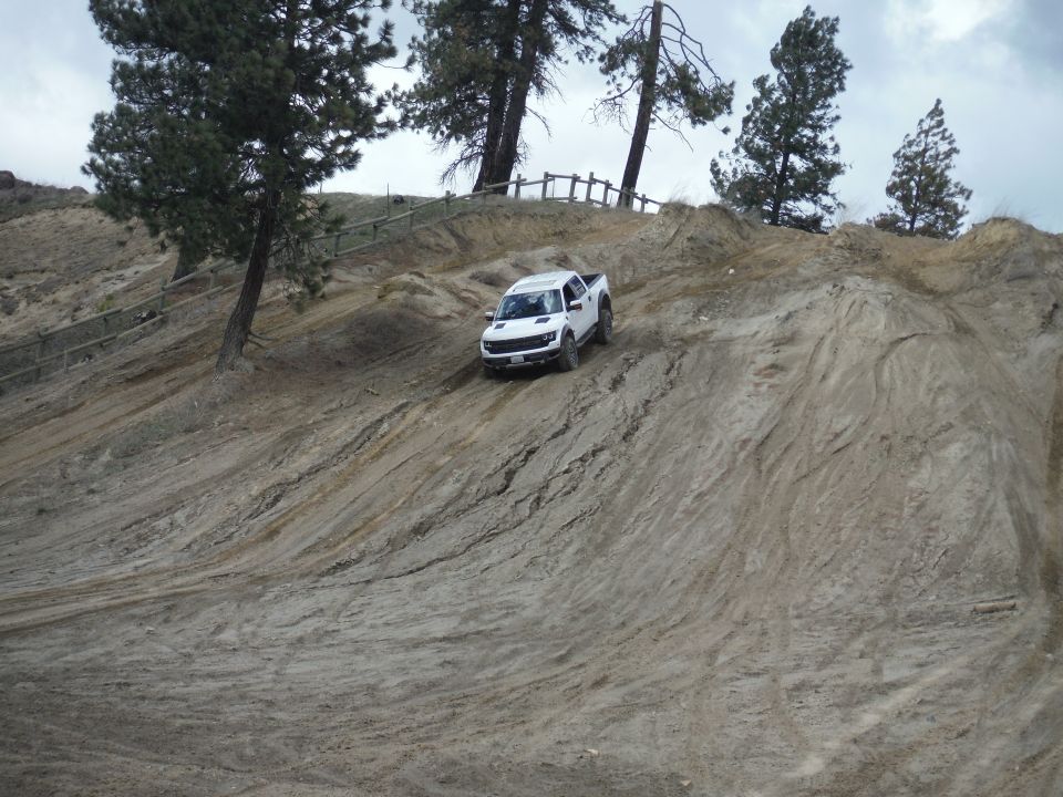 White pickup truck descending a dirt hill, front 3/4 view. The vehicle has a prominent grille and aggressive tires