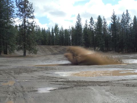 2005 Jeep Wrangler - An off-road vehicle creates a large spray of mud as it drives through a puddle in a wooded, off-road park.