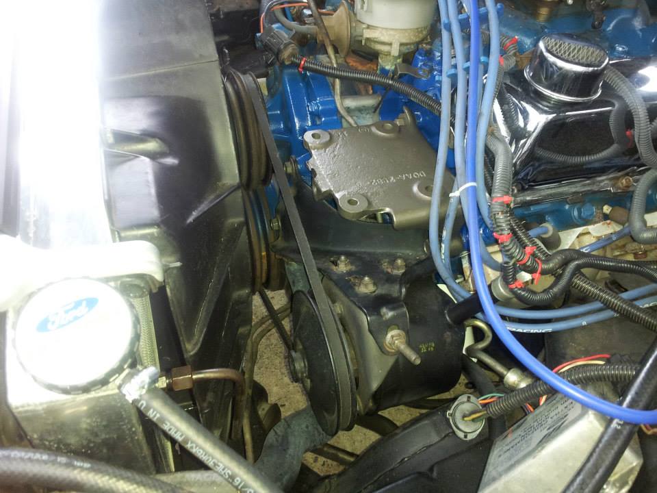 Close-up of a vehicle's engine bay, showing belts, pulleys, blue spark plug wires, and a blue painted engine block