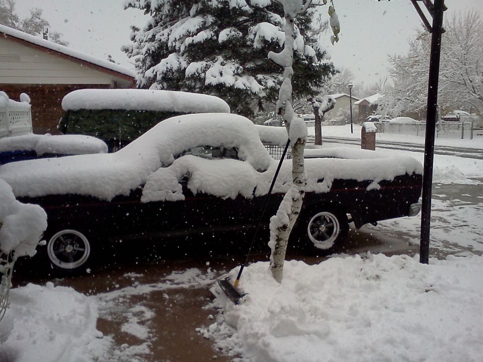 Pickup truck covered in snow with a shovel stuck in a snowdrift