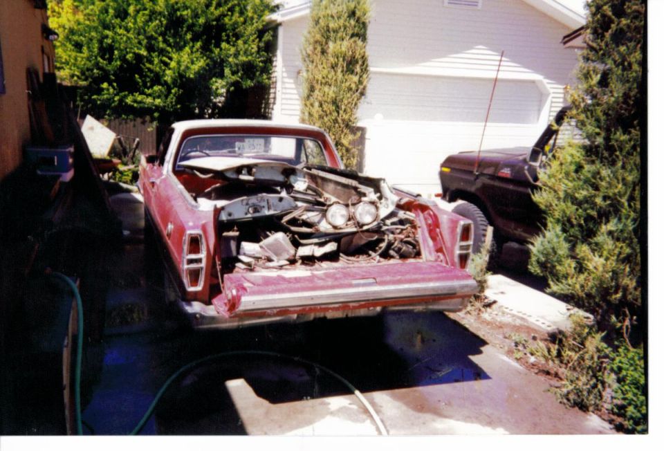 Rear view of red Ford Ranchero in driveway with bed full of disassembled front-end parts and headlights
