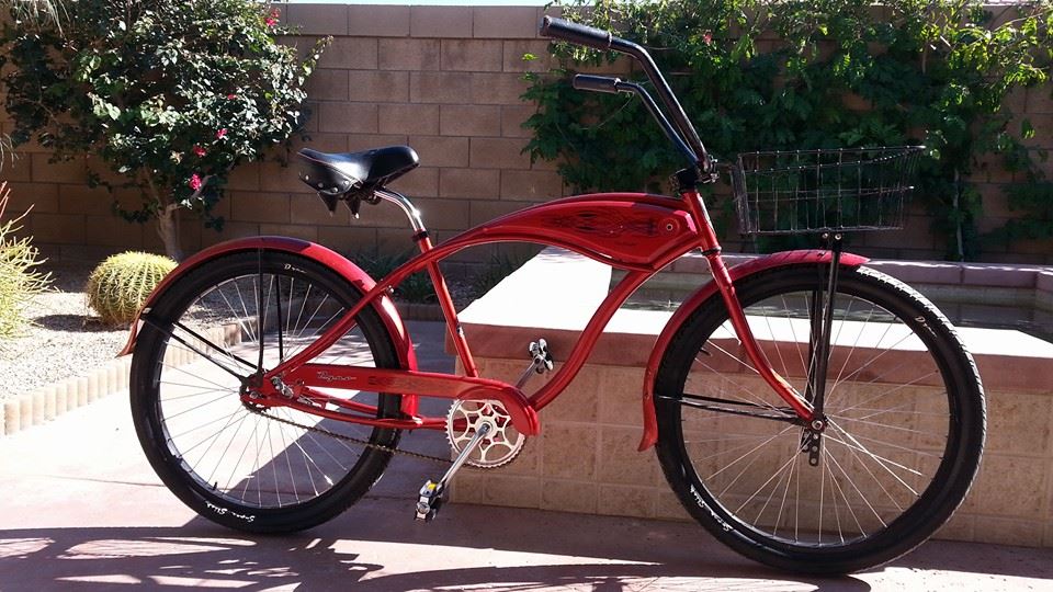 Red cruiser bicycle with a black seat, handlebars, and fenders, and a wire basket on the front