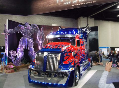 2009 Kenworth T800 - Semi-truck with flame decals displayed with a statue of Optimus Prime.