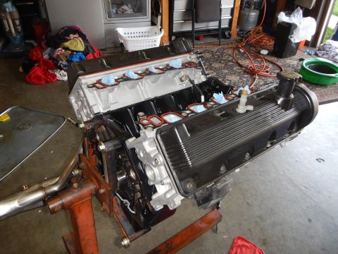 2003 Ford Crown Victoria - V8 engine on a stand in a home garage with laundry and tools behind it, showing aluminum heads, finned valve cover and taped intake ports.