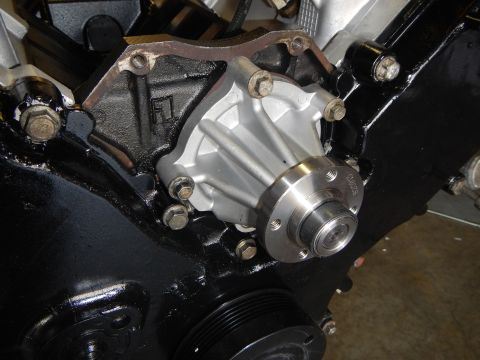 2003 Ford Crown Victoria - fresh aluminum water pump with exposed pulley hub bolted to the black-painted front cover of a V8 engine.